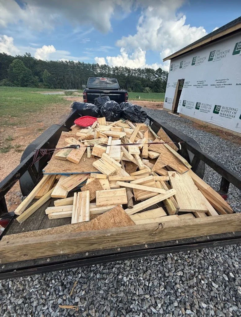 A cleared residential job site in Fredericksburg, VA with a loaded truck ready to haul away a pile of construction debris including lumber scraps, drywall pieces, and roofing material. Anderson Removal LLC crew prepares to transport the waste from a home renovation project.