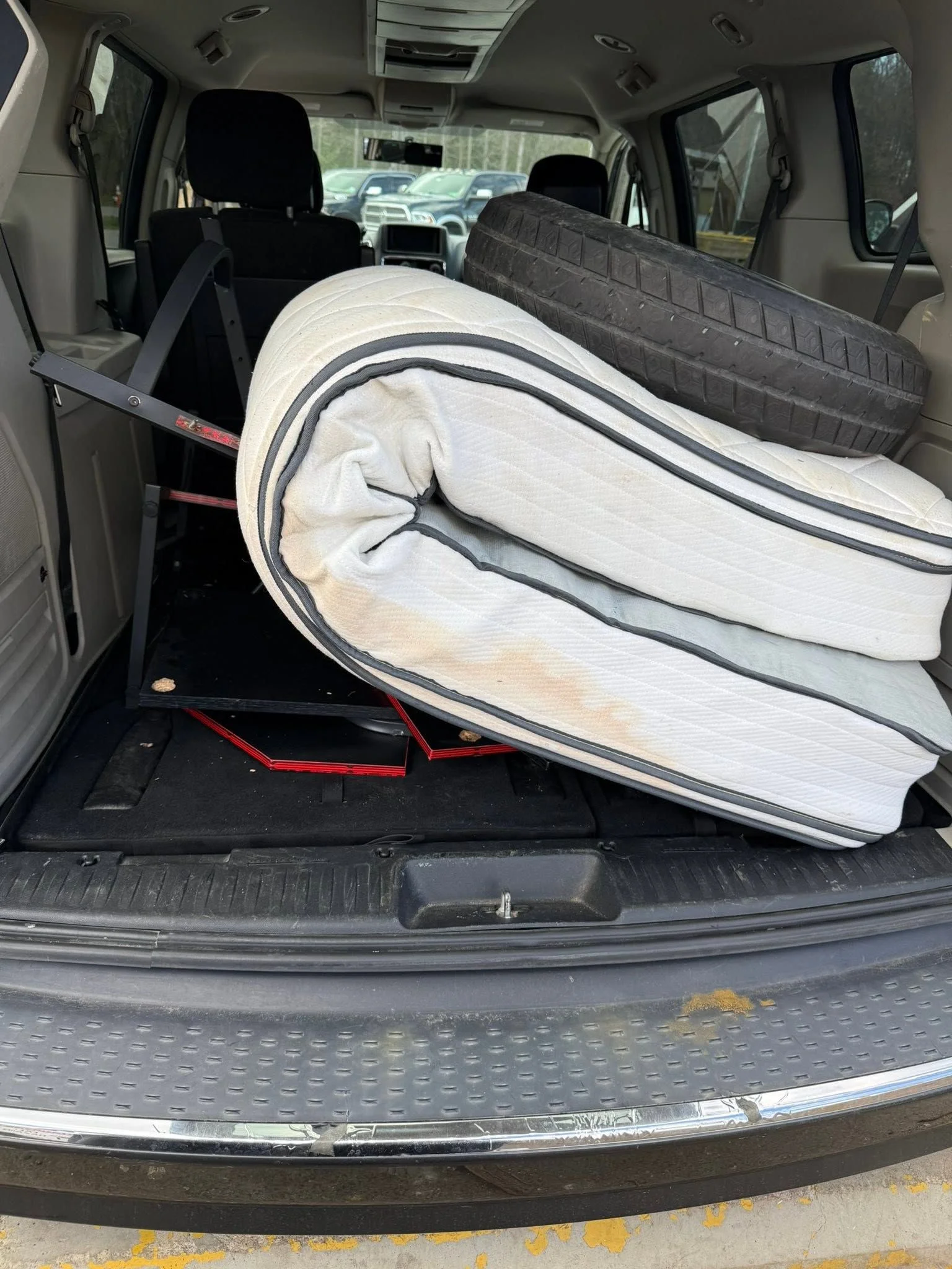An old mattress being carried out of a residential home in Fredericksburg, VA by an Anderson Removal LLC crew member. The mattress is loaded onto a removal truck parked in a suburban driveway.