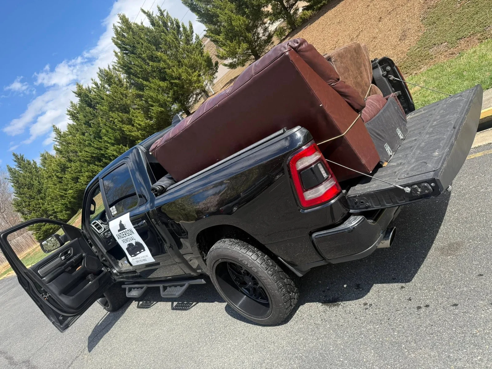 A truck loaded with large furniture and household items being hauled from a residential property in Fredericksburg, VA. An Anderson Removal LLC crew member secures the load in the truck bed before transport.
